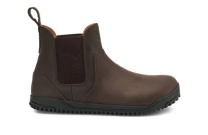 A brown leather Chelsea Boot by Xero Shoes with a black rubber sole, elastic side panel, pull tab at the back, and minimal stitching, shown from the side on a white background—ideal for those seeking a classic style and fit guide.